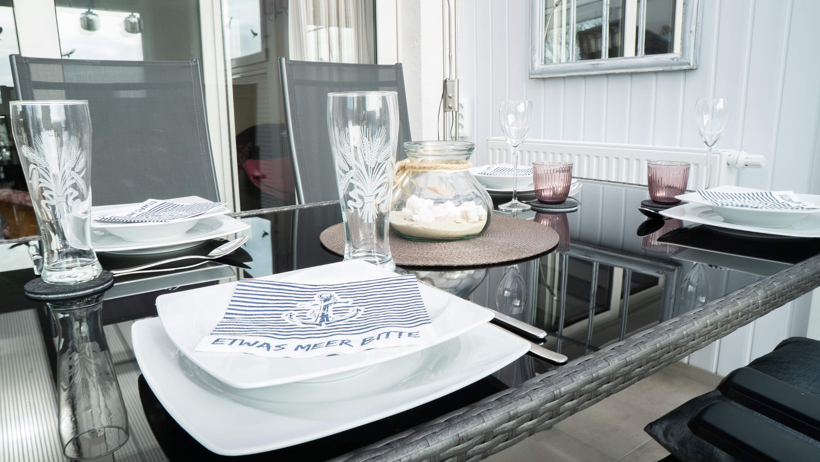 Ein gedeckter Platz am Esstisch mit maritimer Serviette auf dem Teller.